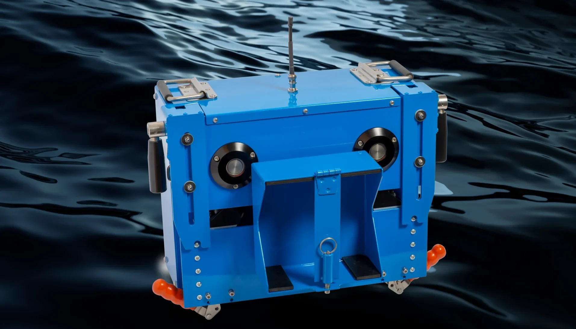 Un vehículo robótico submarino de color azul, con asas y ruedas, está suspendido sobre el agua oscura y ondulante. El dispositivo cuenta con una antena central, múltiples puertos y accesorios metálicos.